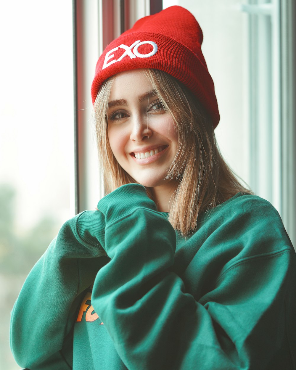 smiling woman in green hoodie wearing red knit cap