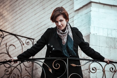 woman in black coat standing beside black metal fence during daytime graceful teams background