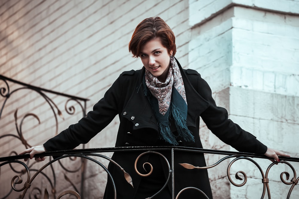 woman in black coat standing beside black metal fence during daytime