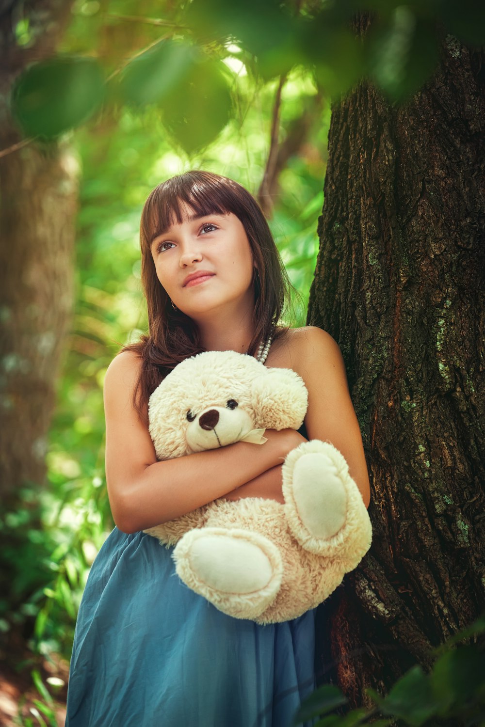 girl in blue sleeveless dress holding white bear plush toy