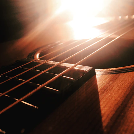 Hands playing an acoustic guitar under warm sunlight.