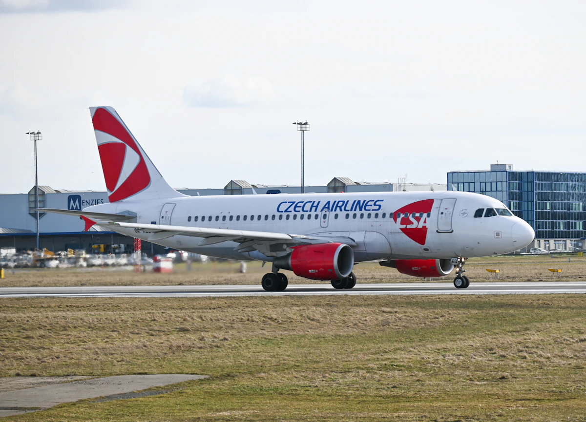 White and red passenger jet parked on an airfield beside a grassy field