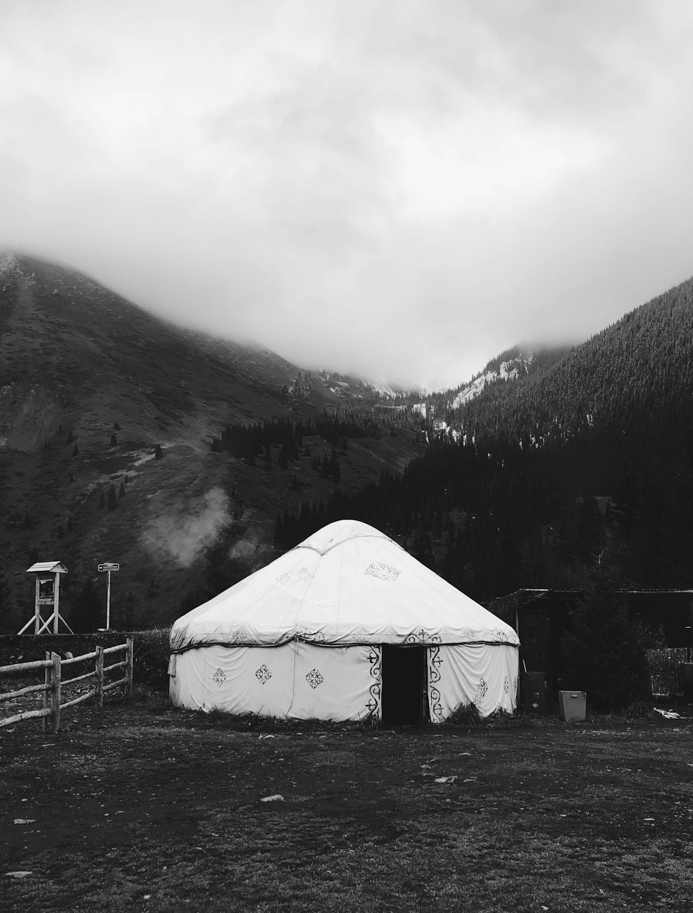 grayscale photo of white tent on green grass field near mountain
