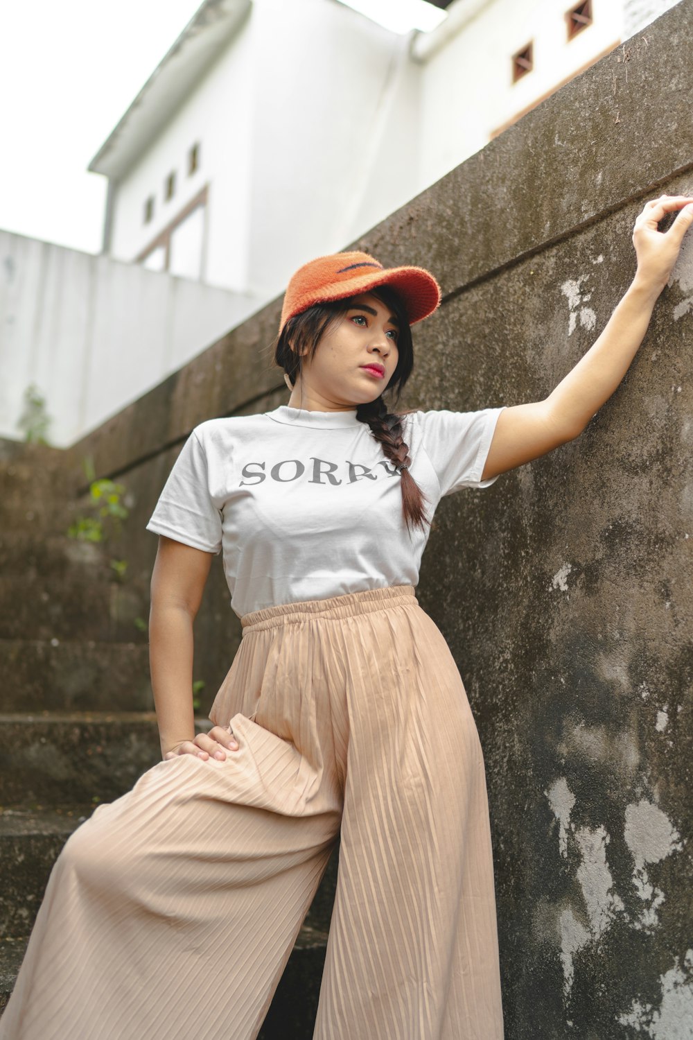 woman in white t-shirt and brown skirt leaning on wall