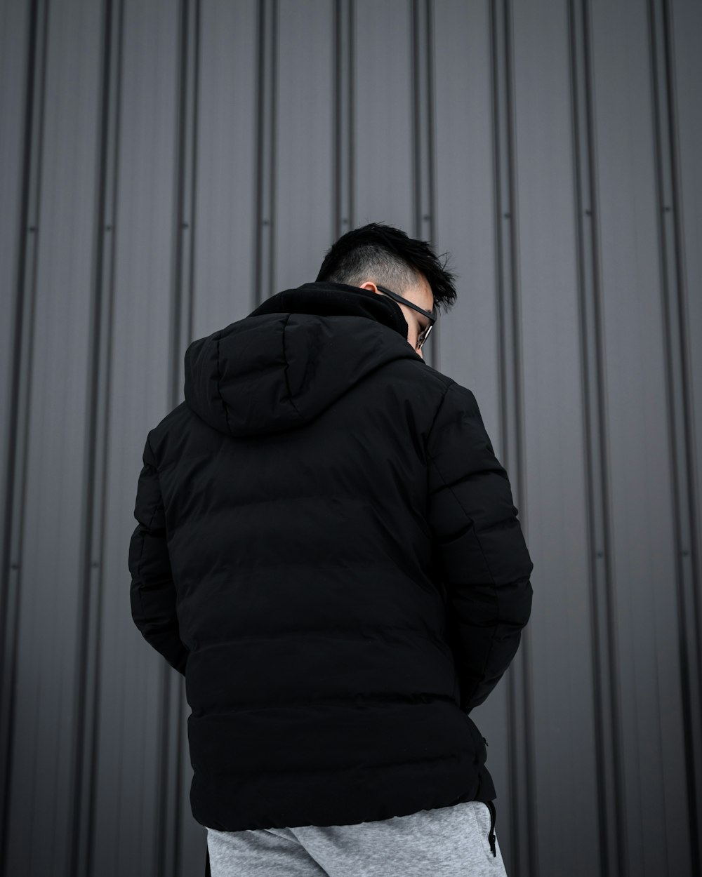 man in black hoodie standing in front of white wall