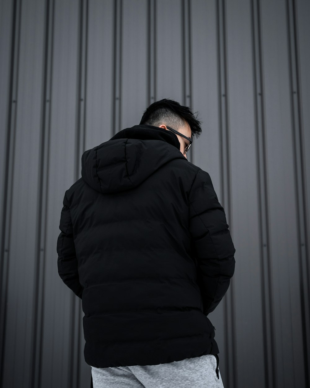 homme en sweat à capuche noir debout devant un mur blanc