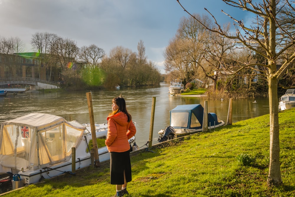 Frau in rosa Jacke steht tagsüber auf grünem Gras in der Nähe von Wasser