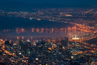 A sweeping aerial shot of Baltimore's Inner Harbor at sunset, showcasing vibrant city lights and water reflections.