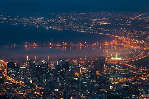 A sweeping aerial shot of Baltimore's Inner Harbor at sunset, showcasing vibrant city lights and water reflections.