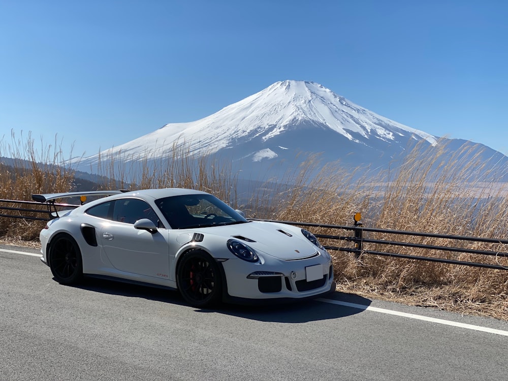 Weißer Porsche 911 tagsüber in der Nähe eines braunen Metallzauns geparkt