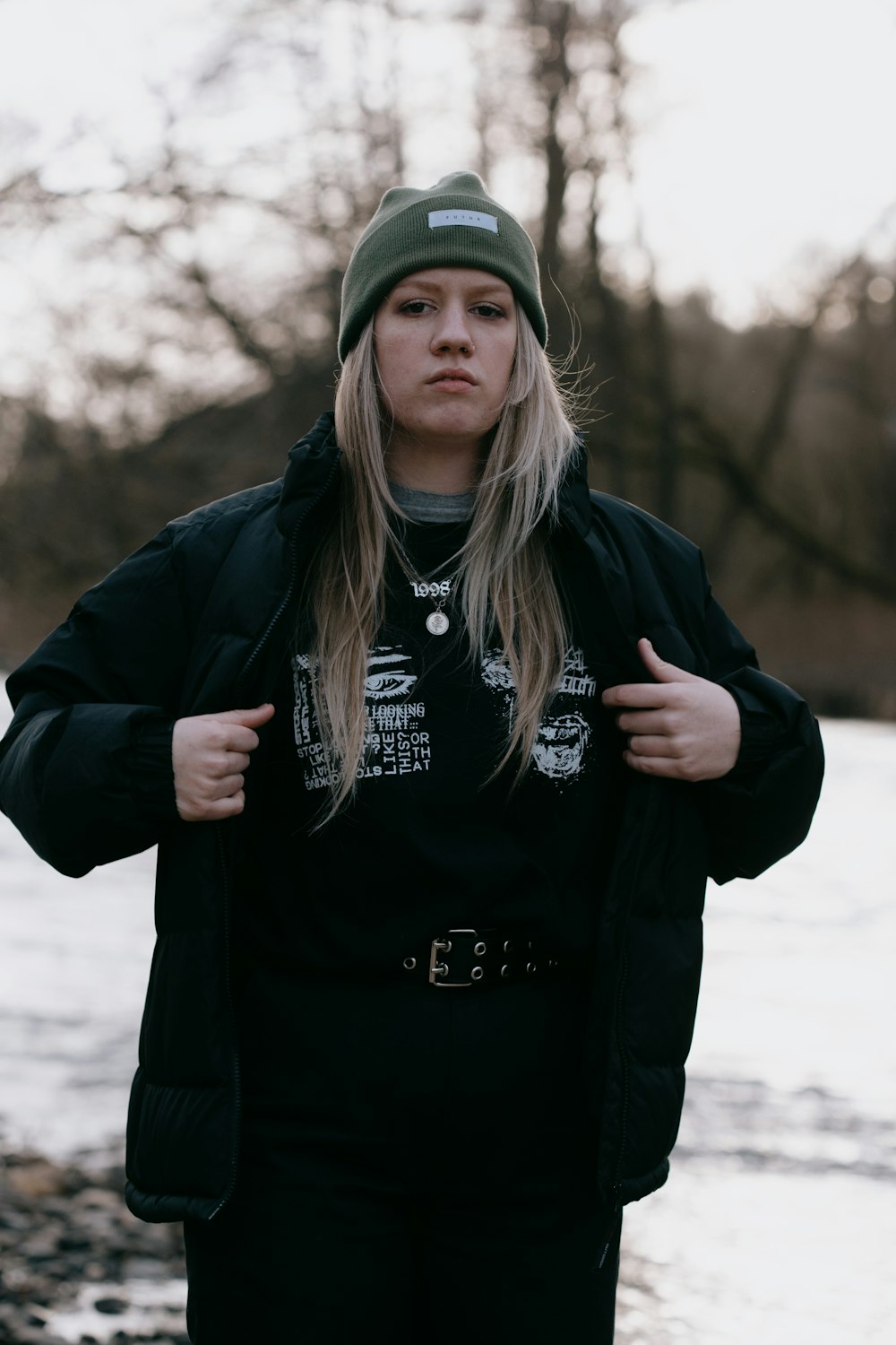 Mujer con chaqueta negra y gorra verde de pie en un suelo cubierto de nieve durante el día