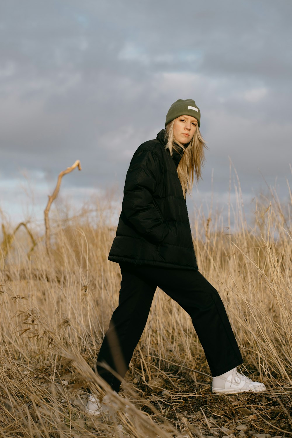 Femme en veste noire et pantalon noir debout sur un terrain d’herbe brune pendant la journée