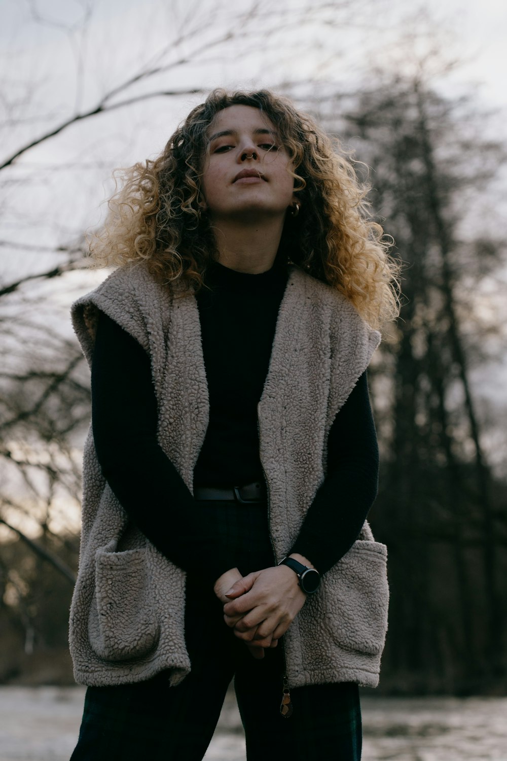 woman in black and gray coat standing near bare trees during daytime