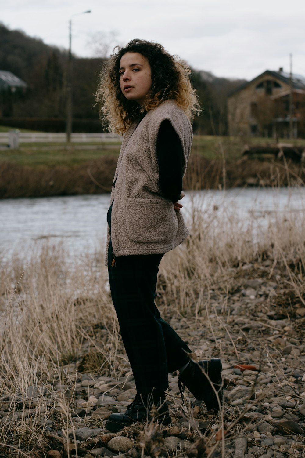 Mujer con suéter gris y pantalones negros de pie cerca del lago durante el día