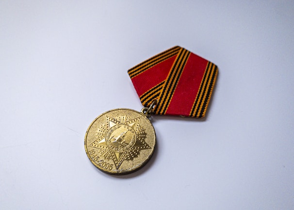 A gold commemorative medal attached to a ribbon with black and orange stripes. The medal features an engraved design with a star shape and buildings or landmarks in the center. It includes the dates 1945-2005, indicating an anniversary or celebration.