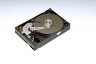 A mechanical hard drive with its metallic platters, actuator arm, and spindle visible. The drive is positioned on a white background, highlighting the intricate details of its components.