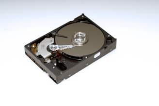 A mechanical hard drive with its metallic platters, actuator arm, and spindle visible. The drive is positioned on a white background, highlighting the intricate details of its components.