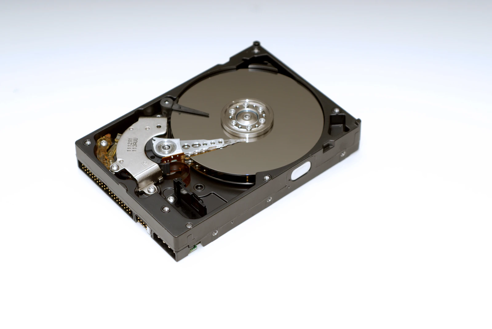 An open hard disk drive on a white background, showing the mirrored platter, read/write actuator arm, and internal mechanics with no visible brand text
