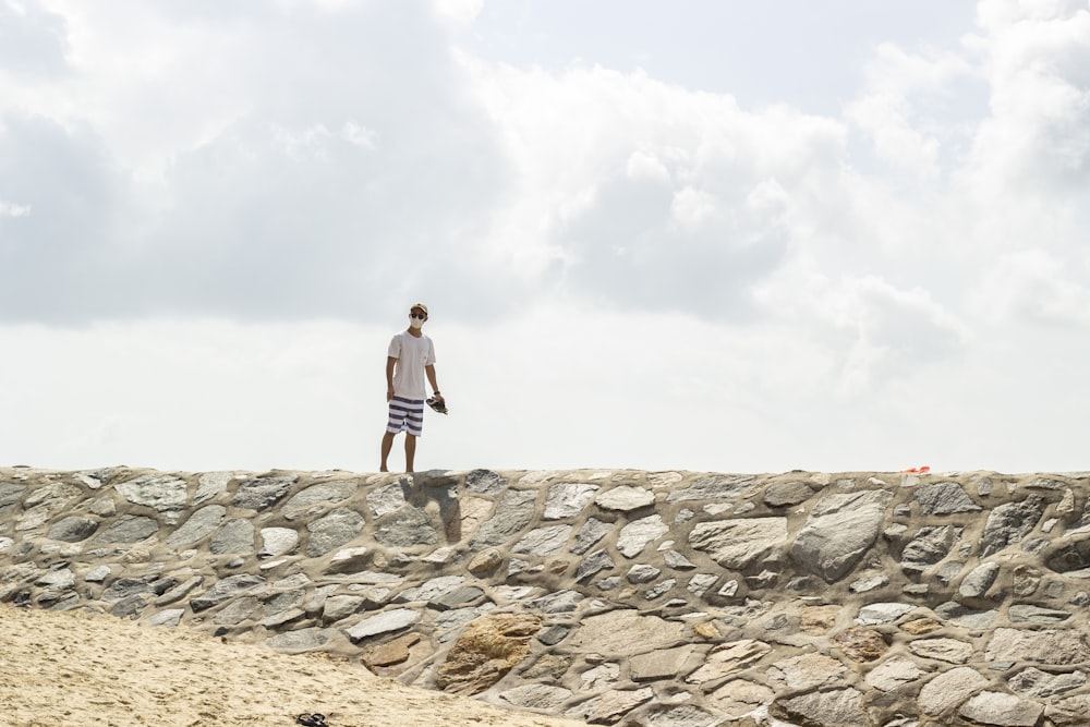 woman in white tank top and black shorts standing on rocky hill under white clouds during