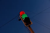 A traffic light with a red and green light illuminated, positioned against a deep blue sky. Electrical wires stretch across the background, connecting to the traffic light.