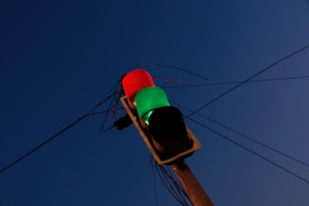 A traffic light with a red and green light illuminated, positioned against a deep blue sky. Electrical wires stretch across the background, connecting to the traffic light.