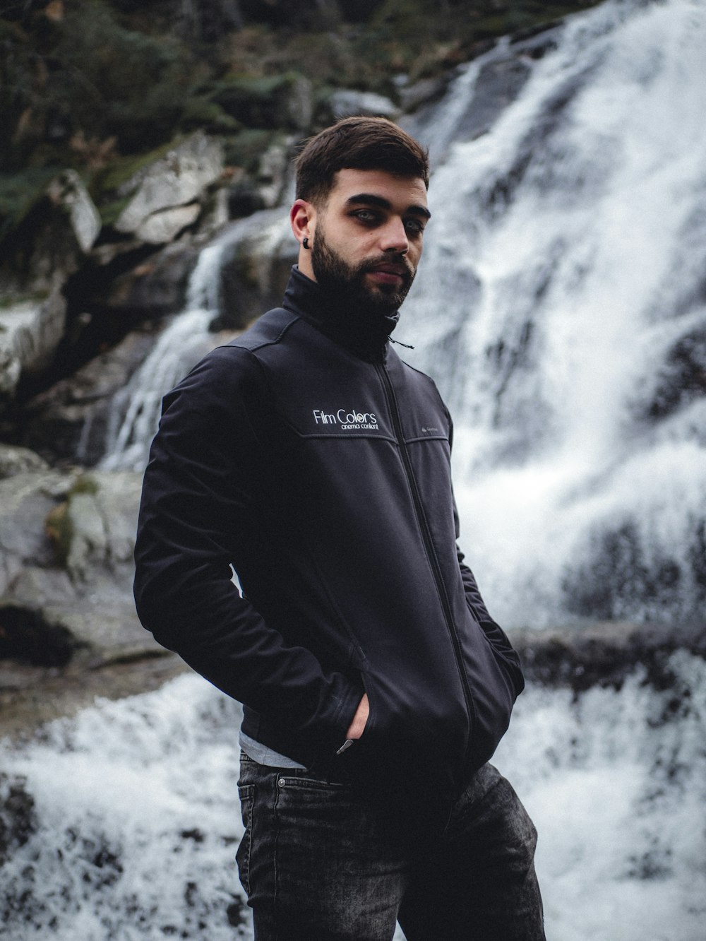 man in black leather jacket standing near waterfalls