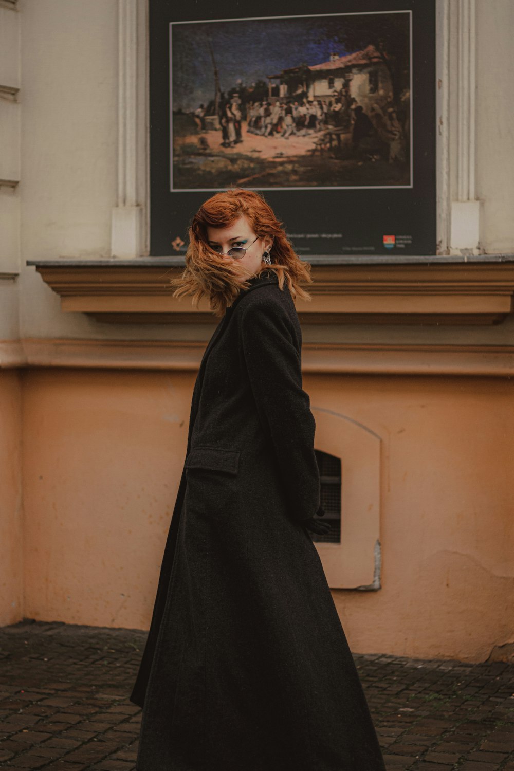 woman in black coat standing near brown wall