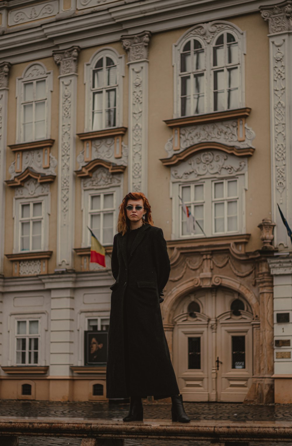 mulher no vestido preto de manga comprida em pé na frente do edifício de concreto marrom durante o dia