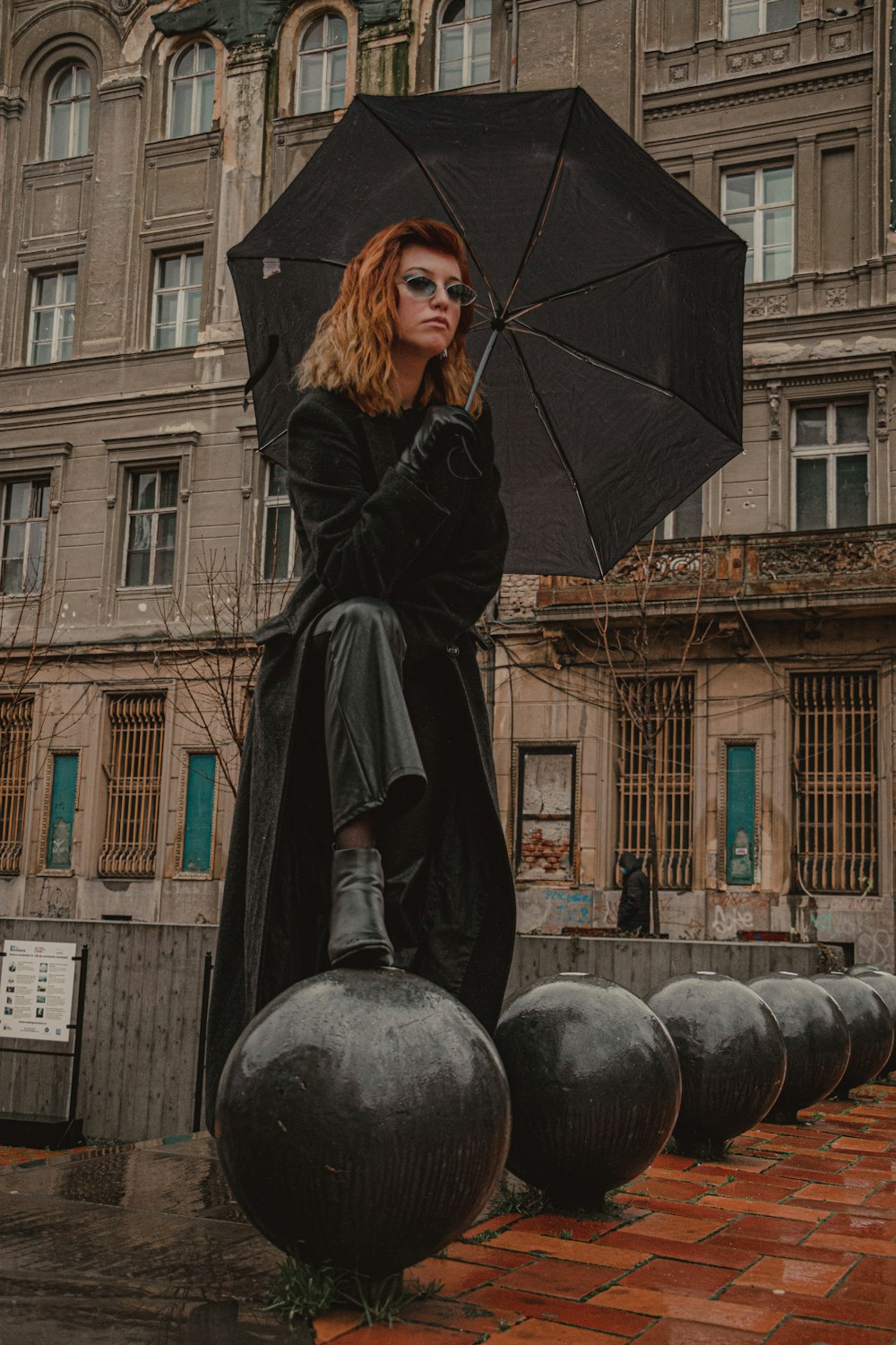 woman in black coat holding umbrella standing near brown concrete building during daytime