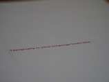 A minimalistic design featuring a piece of paper with the text 'Typography is what language looks like.' written in red ink. The focus on the text gives a stylish and modern feel with ample white space around it.