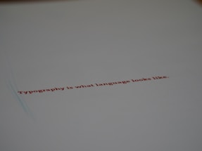 A minimalistic design featuring a piece of paper with the text 'Typography is what language looks like.' written in red ink. The focus on the text gives a stylish and modern feel with ample white space around it.