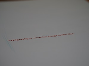 A minimalistic design featuring a piece of paper with the text 'Typography is what language looks like.' written in red ink. The focus on the text gives a stylish and modern feel with ample white space around it.