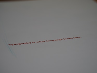 A minimalistic design featuring a piece of paper with the text 'Typography is what language looks like.' written in red ink. The focus on the text gives a stylish and modern feel with ample white space around it.