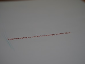 A minimalistic design featuring a piece of paper with the text 'Typography is what language looks like.' written in red ink. The focus on the text gives a stylish and modern feel with ample white space around it.