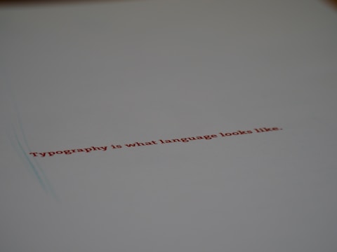 A minimalistic design featuring a piece of paper with the text 'Typography is what language looks like.' written in red ink. The focus on the text gives a stylish and modern feel with ample white space around it.