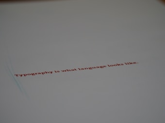 A minimalistic design featuring a piece of paper with the text 'Typography is what language looks like.' written in red ink. The focus on the text gives a stylish and modern feel with ample white space around it.
