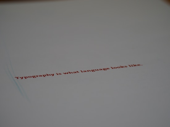 A minimalistic design featuring a piece of paper with the text 'Typography is what language looks like.' written in red ink. The focus on the text gives a stylish and modern feel with ample white space around it.