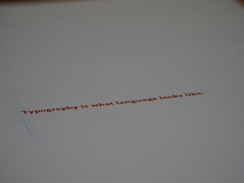 A minimalistic design featuring a piece of paper with the text 'Typography is what language looks like.' written in red ink. The focus on the text gives a stylish and modern feel with ample white space around it.