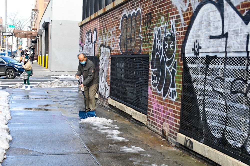Hombre con chaqueta negra y jeans de mezclilla azul de pie junto a la pared con graffiti durante el día