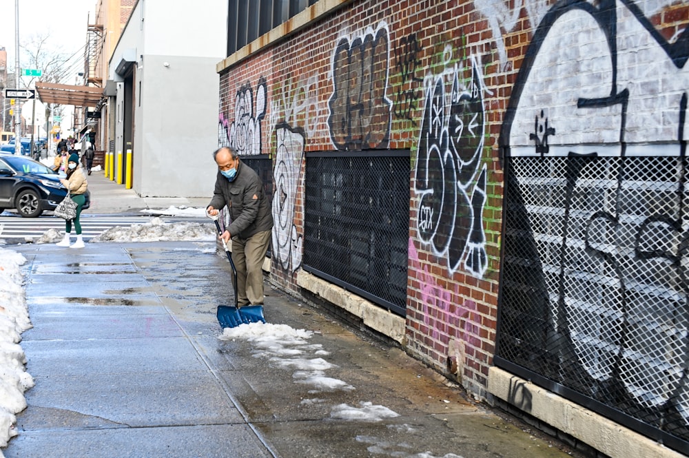 Homme en veste noire et jean bleu debout à côté du mur avec des graffitis pendant la journée