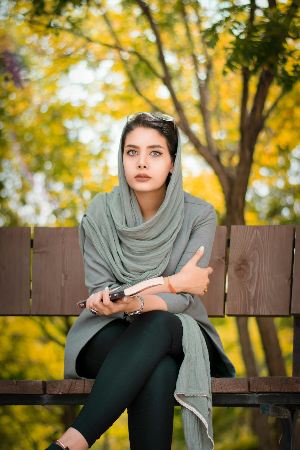 Frau in grauem Hijab und schwarzen Leggings sitzt auf brauner Holzbank