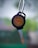 A close-up of a metallic key with a round black plastic grip, displaying the Royal Enfield logo and the text 'Since 1901'. The background is blurred, showcasing a mix of green and neutral tones.