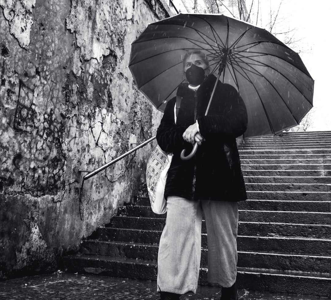 grayscale photo of woman in black jacket and white skirt holding umbrella