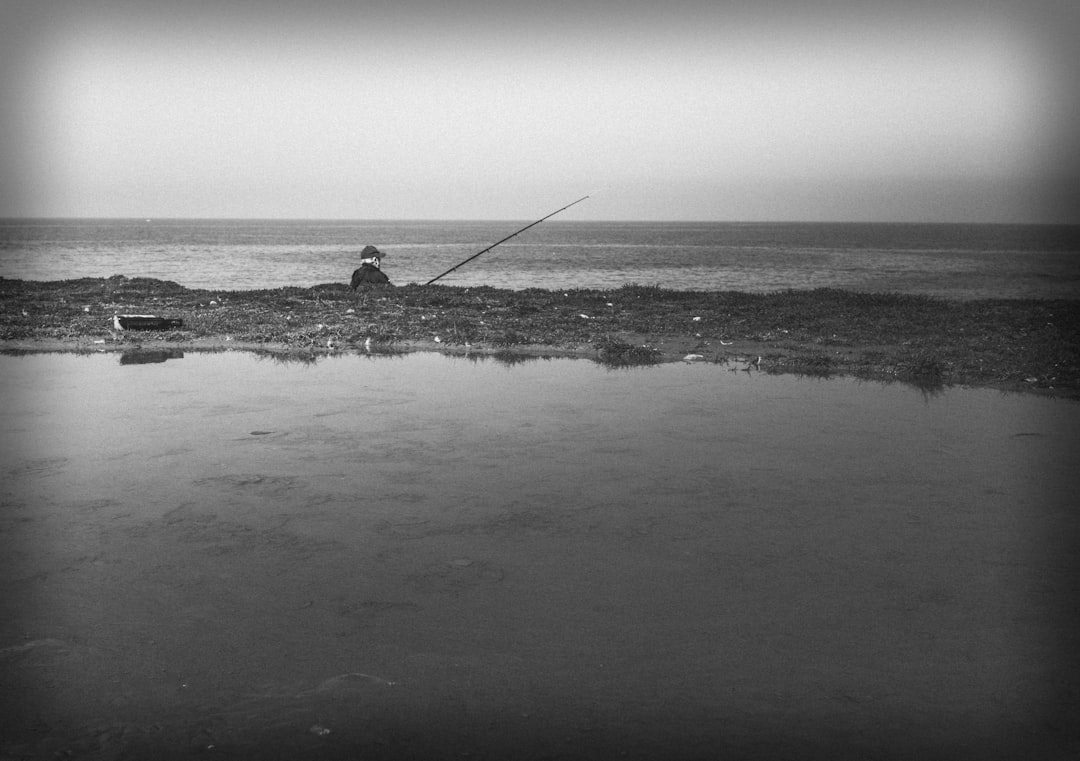 grayscale photo of man fishing on sea
