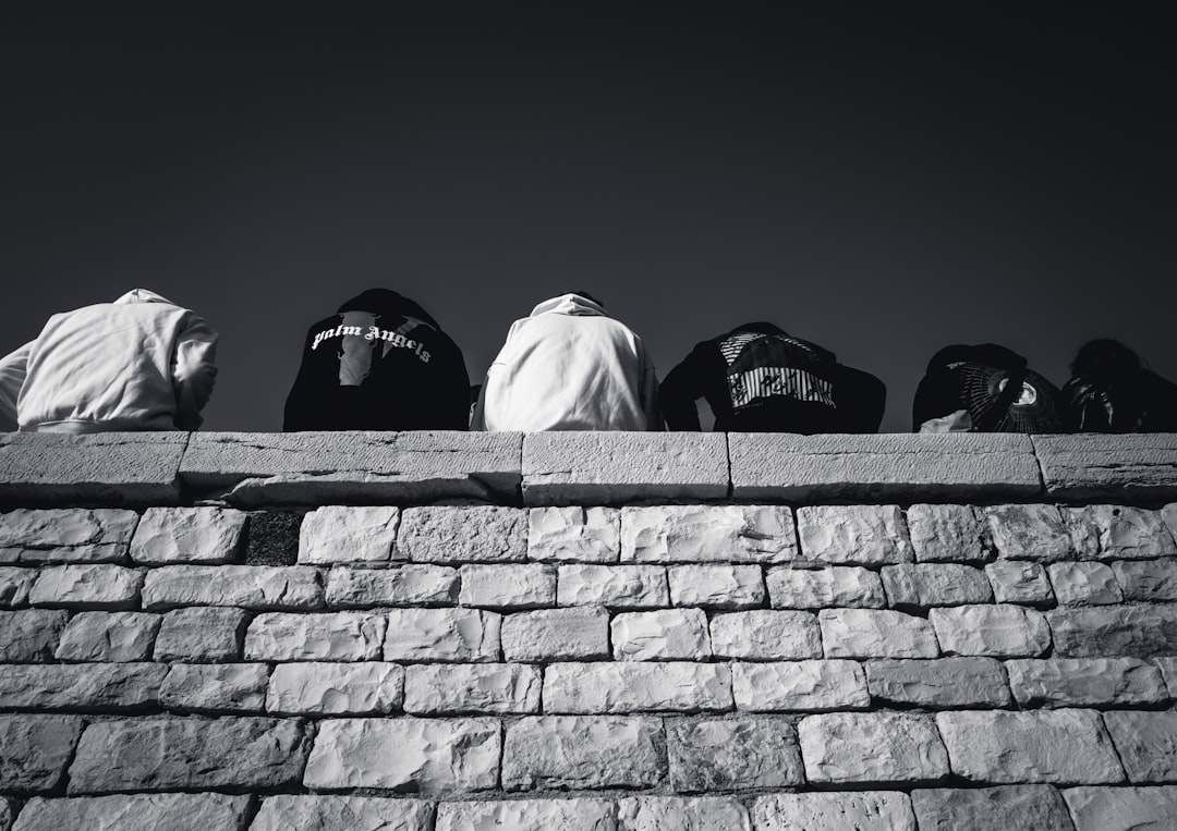 person in white hoodie sitting on gray concrete wall during daytime