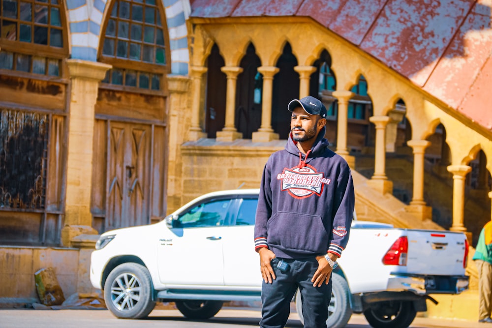 man in blue and white pullover hoodie standing beside white car