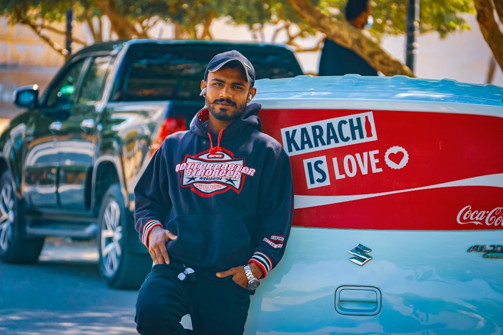 man in red and white pullover hoodie and black pants sitting on white car during daytime