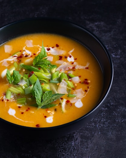Tigela de sopa cremosa de abóbora com gengibre, decorada com creme e salsinha, em ambiente acolhedor