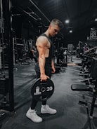man in black tank top holding black dumbbell