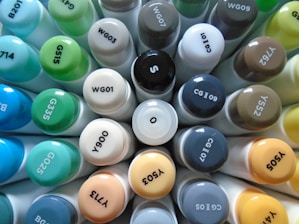 A collection of various colored marker caps arranged in a circular formation, displaying a range of color codes. The caps are tightly packed together, showcasing a spectrum of shades from blues and greens to grays and browns.